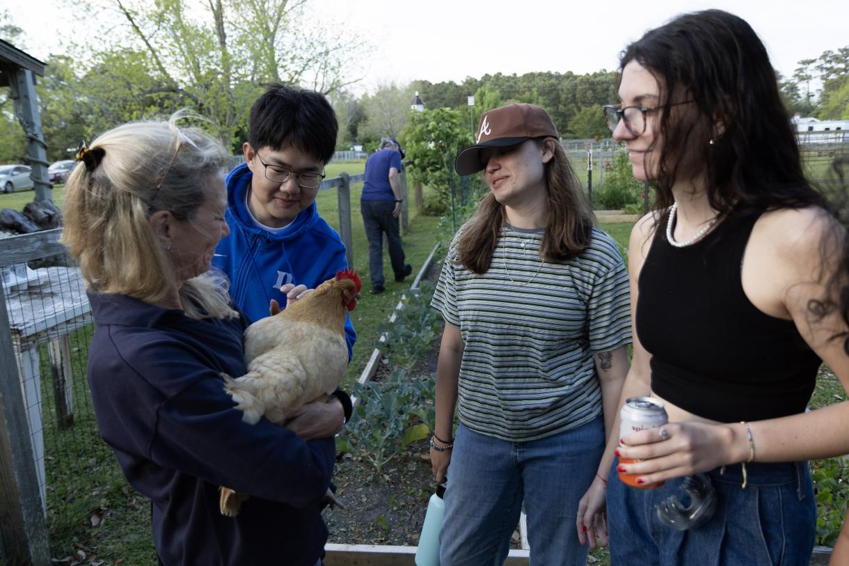 Student stand in garden with a woman holding a chicken.